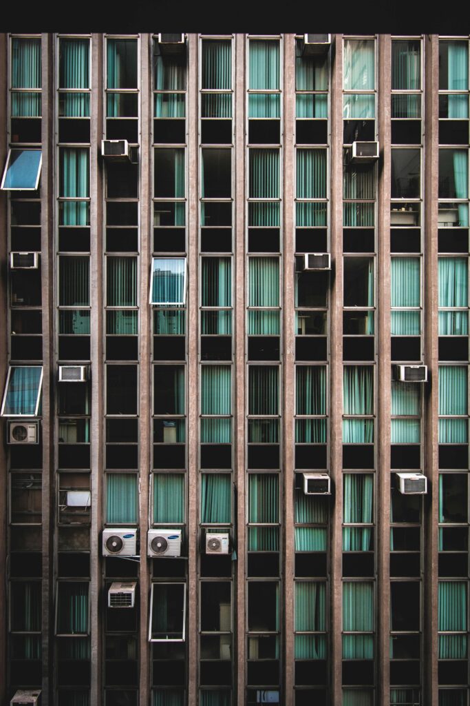 A modern building facade featuring vertical lines and air conditioners, contrasting with green tinted windows.